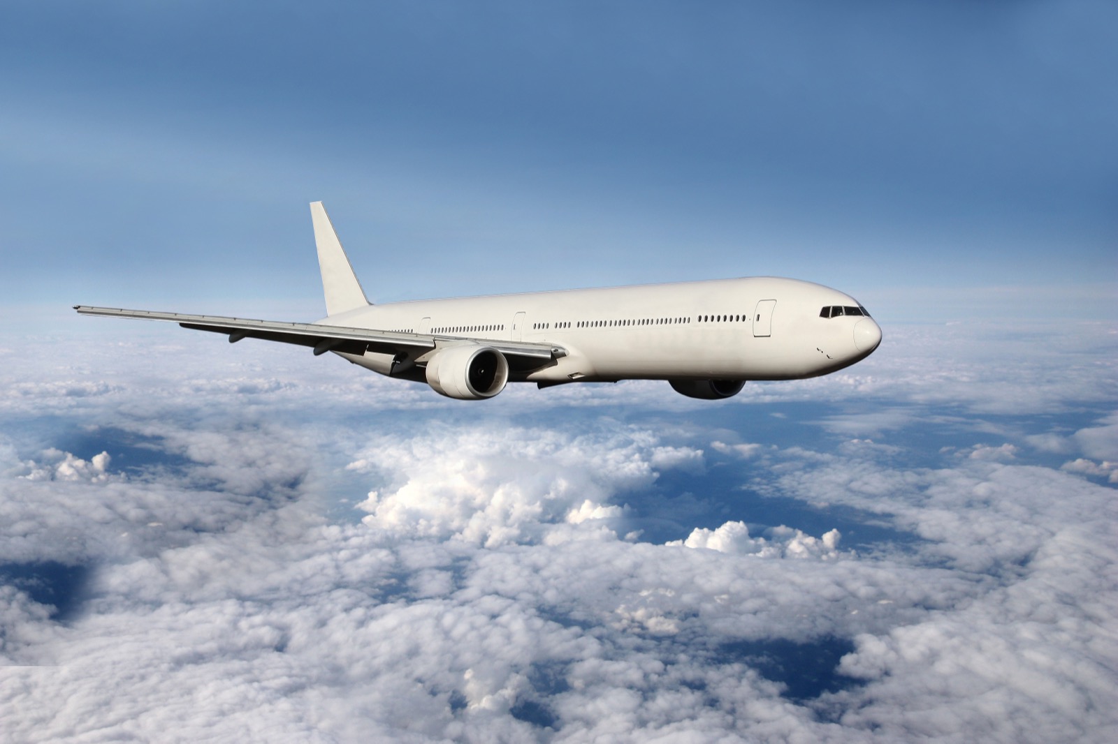 A white twin-engine widebody airliner in the cruise above a layer of cloud